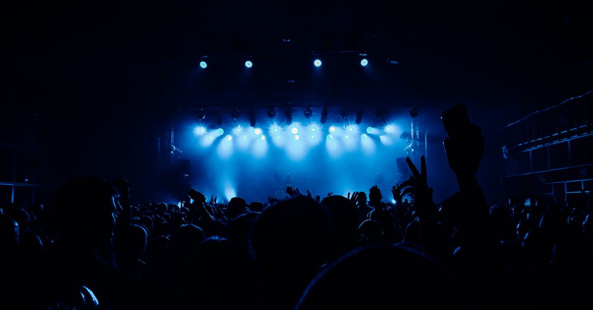 A vibrant concert scene with a lively crowd and dramatic blue stage lighting.